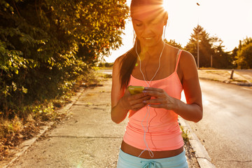 Female jogger running and listening to music on her smart phone.Sunset and lens flare effect.