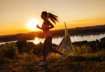 Female runner jogging on beautiful sunset. City scape in background. - obrazy, fototapety, plakaty