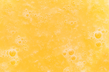 Close-up of bubbles in an yellow orange juice drink.