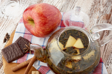 Ripe apple, cinnamon and fruit drink in glass teapot on wooden