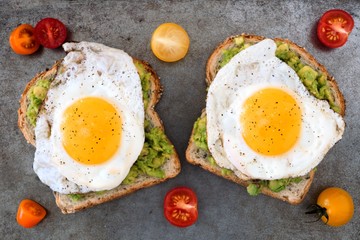 Open avocado, egg sandwiches on whole grain bread with tri-colored tomatoes on rustic baking tray