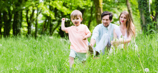 Little boy running over meadow with family in back