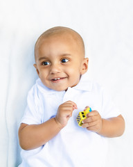 Portrait of cute adorable smiling laughing little indian mixed race infant boy in white shirt on white background playing with car toy 