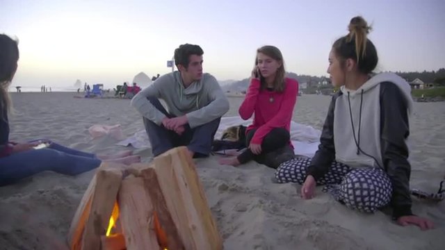 Cute girl talks on her cell phone while sitting with friends by the fire 