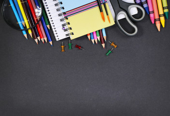 notebook, exercise book, scissors and pencils on black board bac