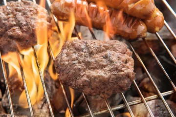 Crédence de cuisine en verre imprimé Grill / Barbecue Beef burger and sausages cooking over flames on grill
