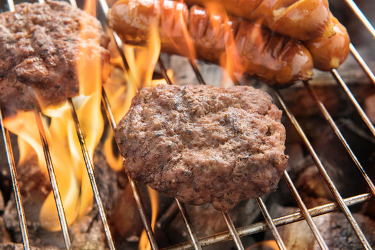 Beef burger and sausages cooking over flames on grill