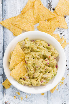 spicy avocado sauce and corn chips on white wooden background