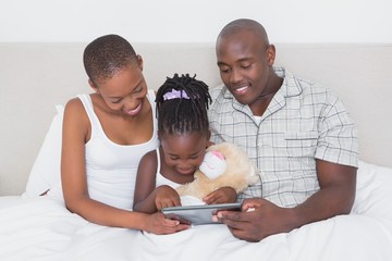 Fototapeta premium Pretty couple using tablet with their daughter in bed 