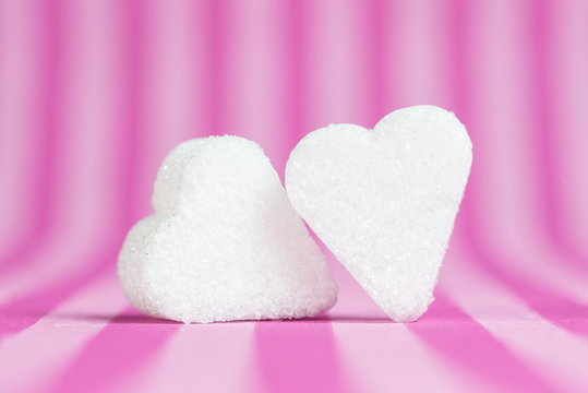 Two white sugar hearts isolated on pink striped background.