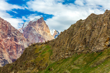 Mountain landscape with unusual perspective.
Bright color layers of highland formation with grassy ridge on foreground and red orange rocky wall on background with glaciers and snow on top of peak