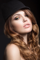 Beautiful girl with bright makeup and curls in a hat. Beauty face. Picture taken in the studio on a black background.