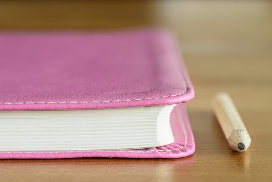 Pink leather notebook with pencil.