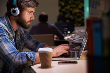 Office Worker With Coffee At Desk Working Late On Laptop
