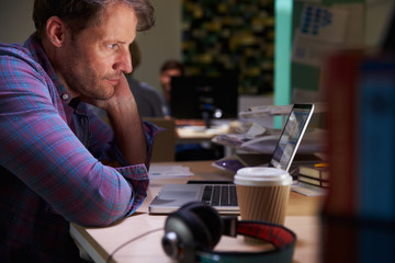 Male Office Worker With Coffee At Desk Working Late