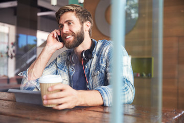 Businessman On Phone Using Digital Tablet In Coffee Shop