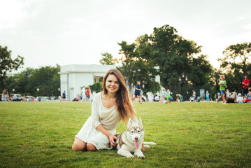 young caucasian female sitting on green grass with siberian husky puppy in the park