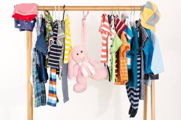 Dressing closet with clothes arranged on hangers.Colorful wardrobe of newborn,kids, toddlers, babies full of all clothes.Many t-shirts,pants, shirts,blouses, onesie on a rack, pink rabbit toy hanging