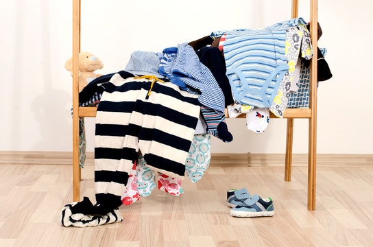 Wardrobe of newborn,kids, toddlers, babies.Many t-shirts,pants, shirts, shoes, hat,blouses, onesie in a pile . Messy clothes thrown on a shelf and a teddy bear