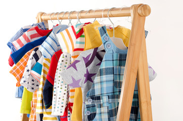 Dressing closet with clothes arranged on hangers.Colorful wardrobe of newborn,kids, toddlers, babies full of all clothes.Many t-shirts,pants, shirts,blouses, onesie hanging