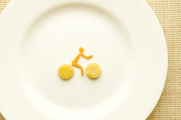 Cyclist from carrots and corn on the white plate