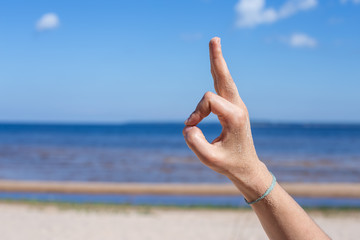 Meditation in nature. Female hand: fingers in the form of yogic gesture against the blue sea and sky.