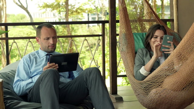 Young business couple with tablet computer and smartphone working on terrace
