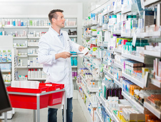 Male Pharmacist Counting Stock While Holding Tablet Computer