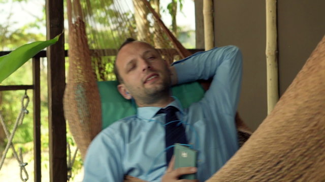 Young businessman singing while listening to music on hammock
