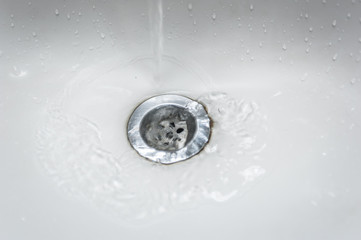 Closeup of tap water flowing into stainless steel drain of white