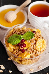 cereal flakes with fresh berries in a bowl, cup of tea and honey