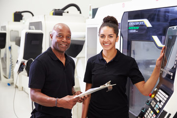 Portrait Of Apprentice Working With Engineer On CNC Machine