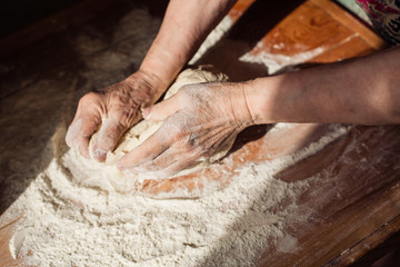 Senior woman hands knead dough on a table in her home kitchen