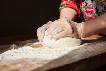 Senior woman hands knead dough on a table in her home kitchen