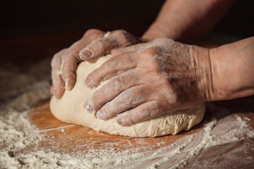 Senior woman hands knead dough on a table in her home kitchen