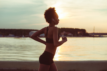 Attractive young African girl athlete running at sunset along the beach. Fitness training of runner.