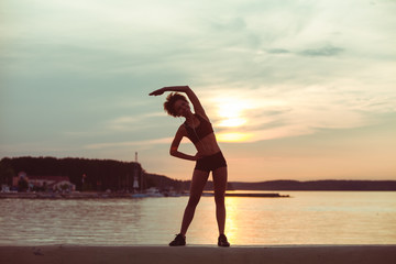 Attractive young African girl silhouette exercising stretching on a beach after running at sunset