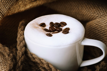 Fresh cappuccino coffee cup with coffee beans on burlap sack