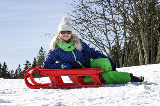 Woman riding a mountain on red sled.