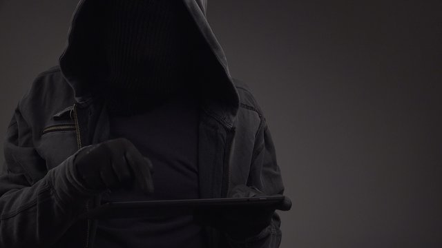 Unrecognizable faceless hooded cyber criminal using digital tablet computer to access internet web page, p2p and piracy concept, 4k uhd footage