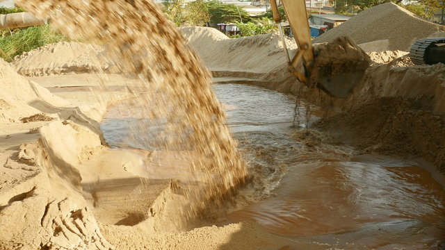 Pipe discharging of dredged river sand to disposal site and excavator in use ( close up )
