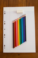 Crayons de couleur multicolores avec une gomme posés sur une feuille perforée à grands carreaux