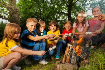 Happy friends near bonfire with marshmallow