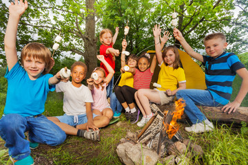 Fototapeta premium Teens with arms up near bonfire hold marshmallow