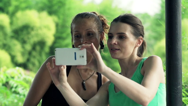 Two happy, beautiful girlfriends taking selfie photo with cellphone
