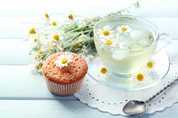 Cup of chamomile tea with chamomile flowers and tasty muffin on color wooden background