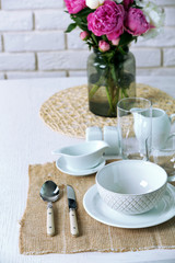Beautiful table setting with flowers in vase on brick wall background