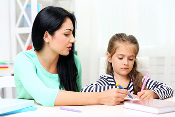 Obraz premium Beautiful school girl doing homework with mother at home