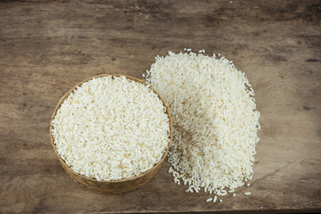 Rice in a wicker rice and scattered near on dark wooden table