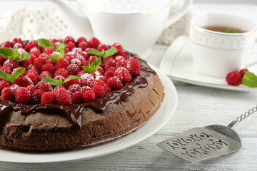 Cake with Chocolate Glaze and raspberries and cup of tea on color wooden background
